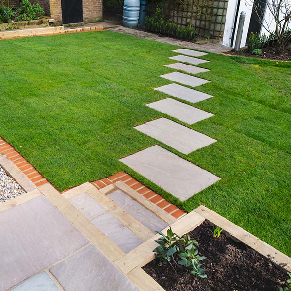 New turf installation around a new stepping stone pathway to a pebbled area and patio with steps. All part of a garden landscaping desing project.