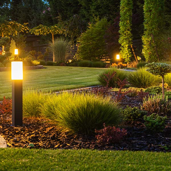 Panoramic Photo of LED Light Posts Illuminated Backyard Garden During Night Hours. Modern Backyard Outdoor Lighting Systems.