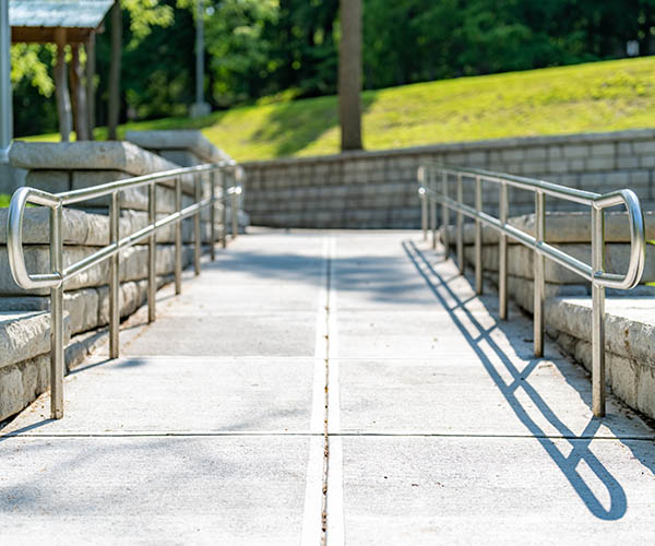 Outdoor, exterior gray concrete ramped sidewalk with stainless steel railings.