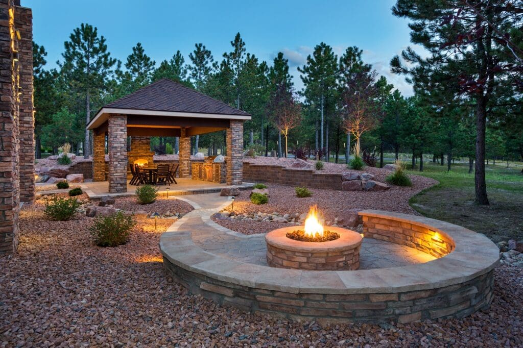 Custom outdoor living space designed by Legacy Landscaping featuring a covered pavilion, fire pit, seating area, landscape lighting, and decorative hardscaping.